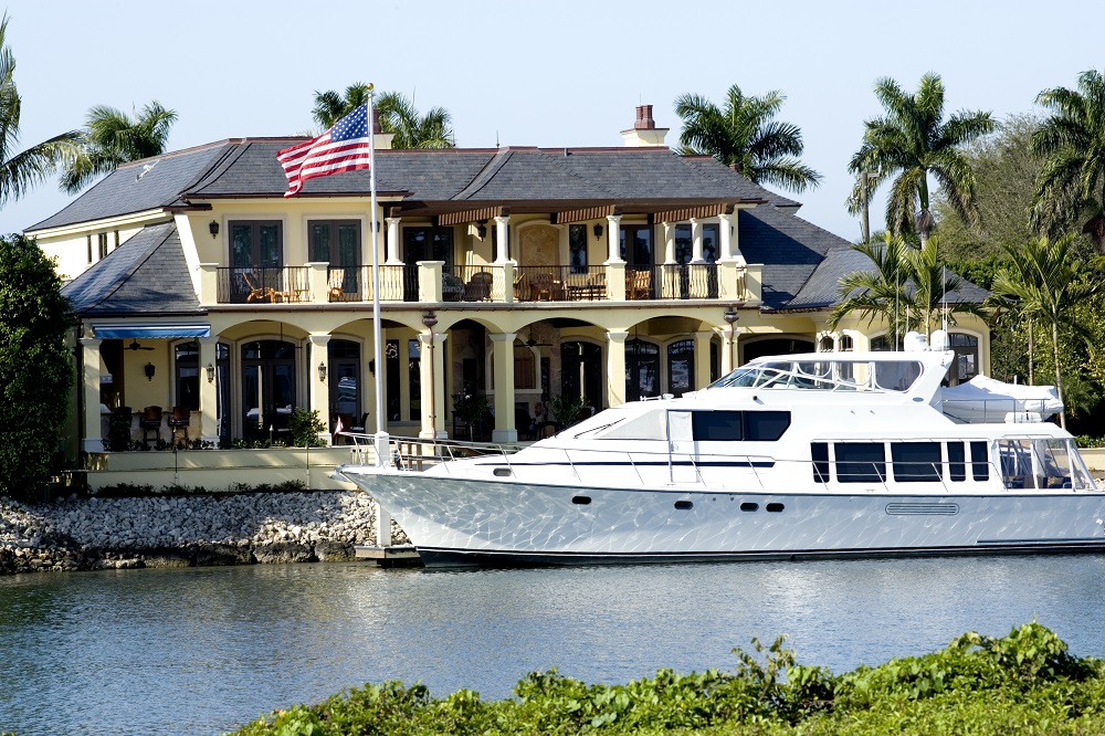 expensive home with yacht in front of it